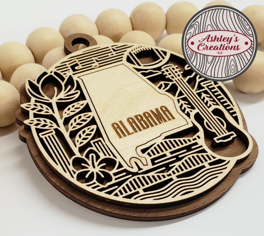 Wooden ornament with 'Alabama' engraving, surrounded by wooden beads, branded 'Ashley's Creations'.