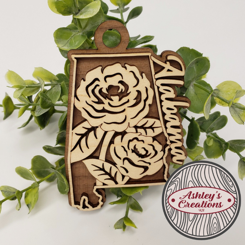 Wooden ornament shaped like the state of Alabama with floral design, surrounded by green leaves. Made by Ashley's Creations KS.