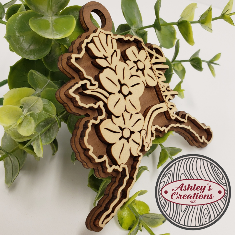Wooden floral design ornament with green leaves in the background, featuring 'Ashley's Creations' logo.