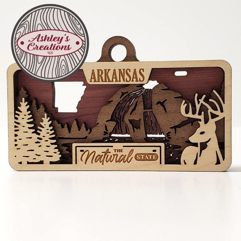 Wooden three layer license plate ornament with 'Arkansas' and nature-themed designs, featuring 'Ashley's Creations' branding.