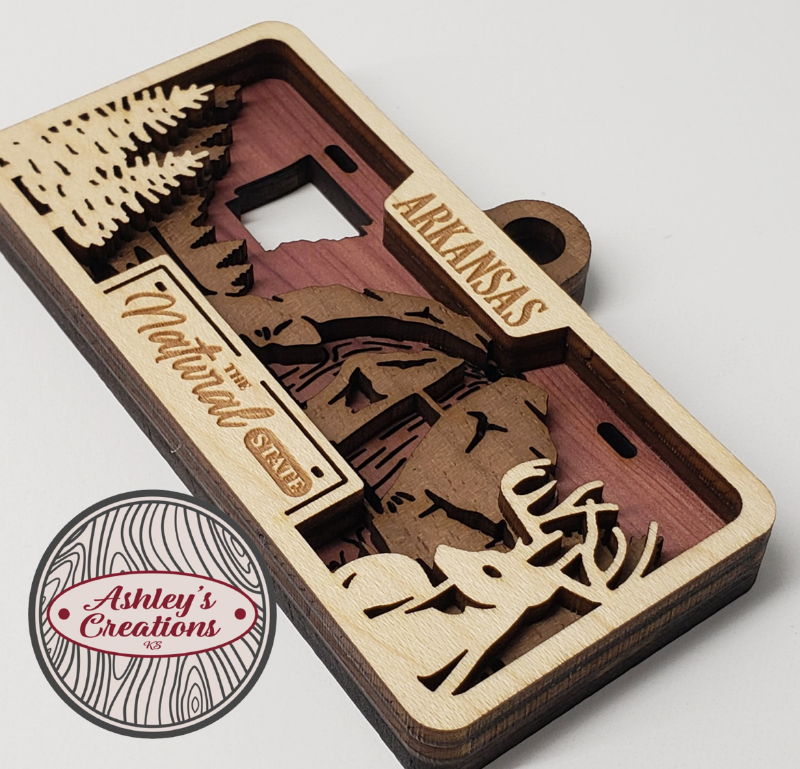 Wooden three layer license plate ornament with laser-cut designs and 'Arkansas' text on a white background