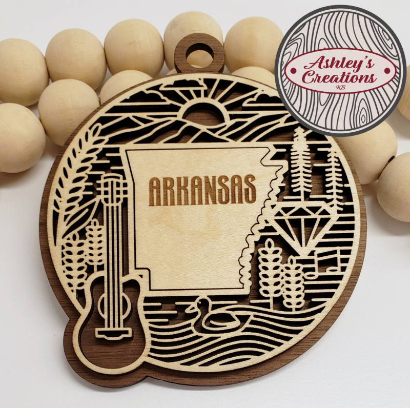 Decorative wooden ornament with 'Arkansas' text and guitar design, surrounded by wooden beads, branded 'Ashley's Creations'.