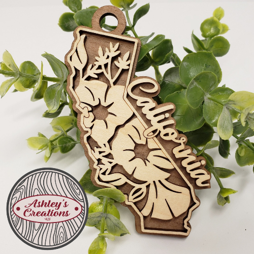 Wooden cutout of California shape with floral designs on a white background with green leaves.