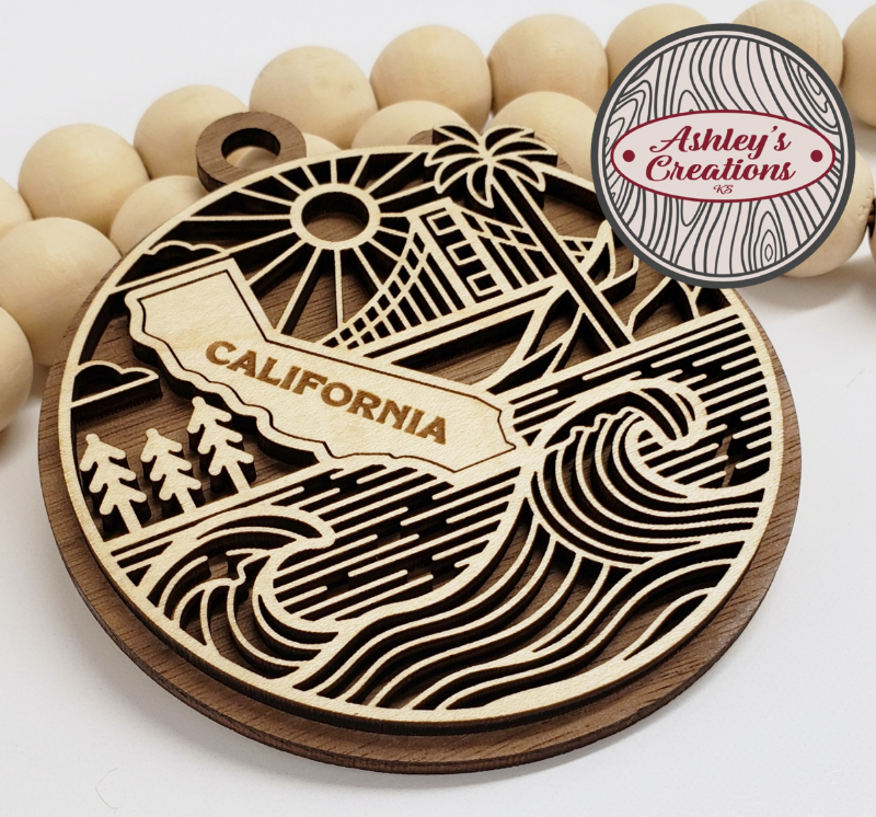 Wooden ornament with 'California' design and palm tree, surrounded by wooden beads, branded 'Ashley's Creations'.