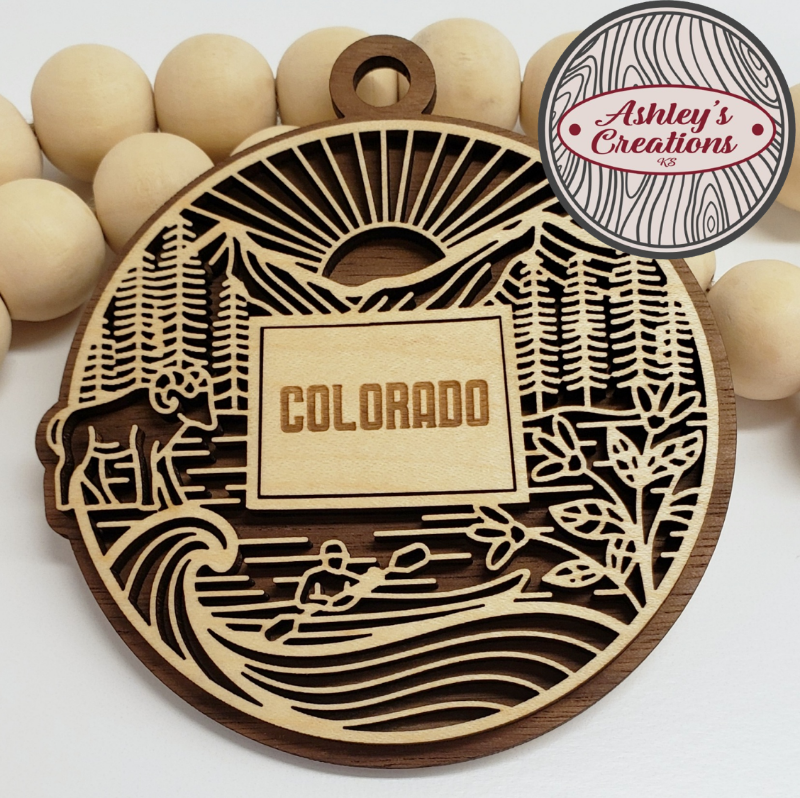 Wooden ornament with 'Colorado' engraving, surrounded by wooden beads, branded 'Ashley's Creations'.