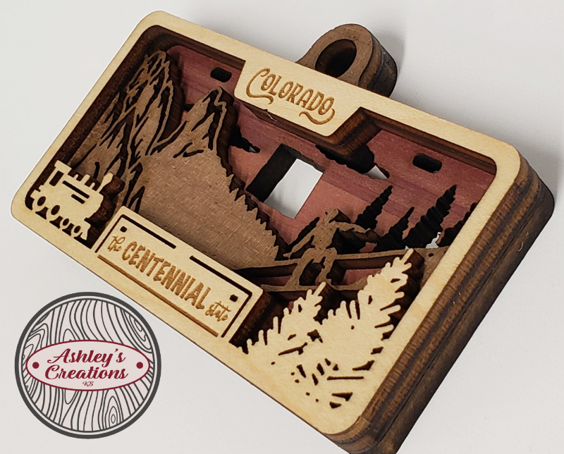 Wooden three layer license plate ornament with laser-cut designs and 'Colorado' text on a white background