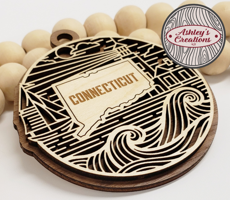 Wooden ornament with 'Connecticut' engraving on a white background, branded 'Ashley's Creations'.