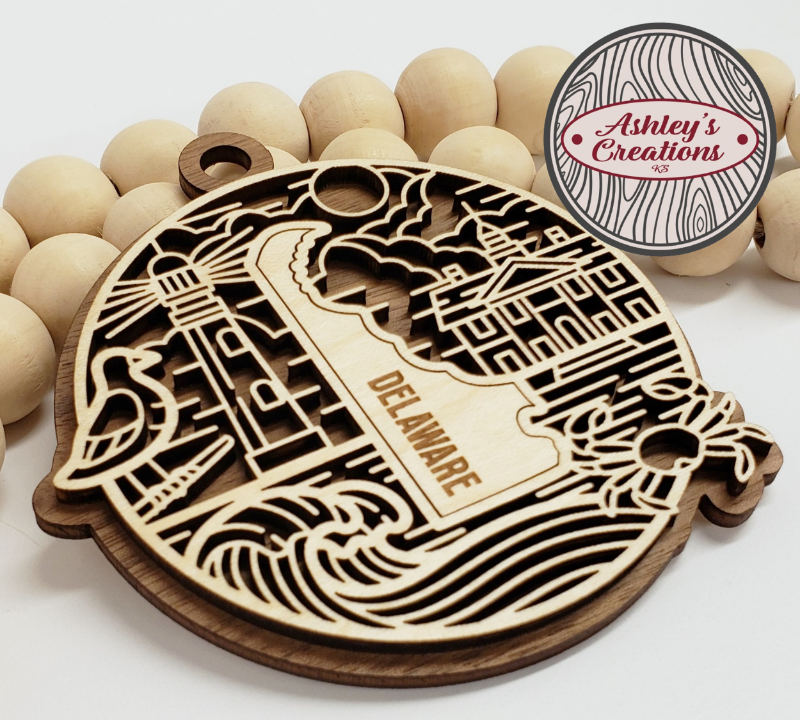 Wooden ornament with 'Delaware' engraving on a white background, branded 'Ashley's Creations'.