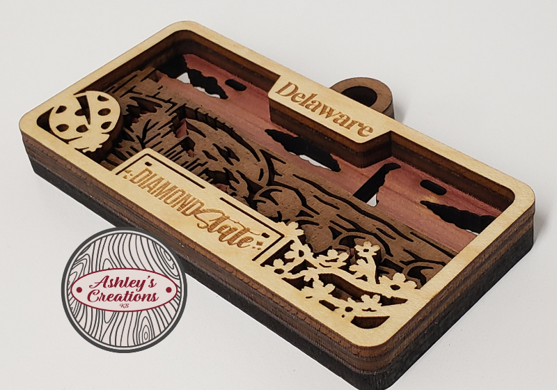 Wooden three layer license plate ornament with laser-cut designs and 'Diamond State' branding on a white background.