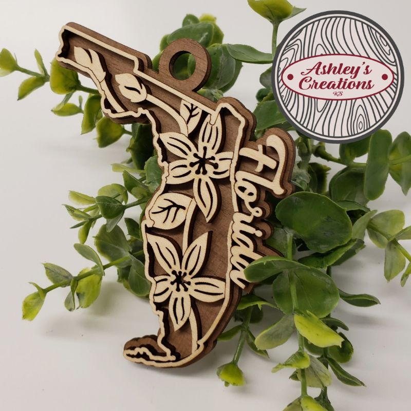 Wooden Florida-shaped ornament with floral designs on a white background with green leaves.
