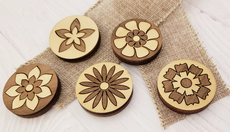 Five wooden magnets with floral designs on a textured fabric background