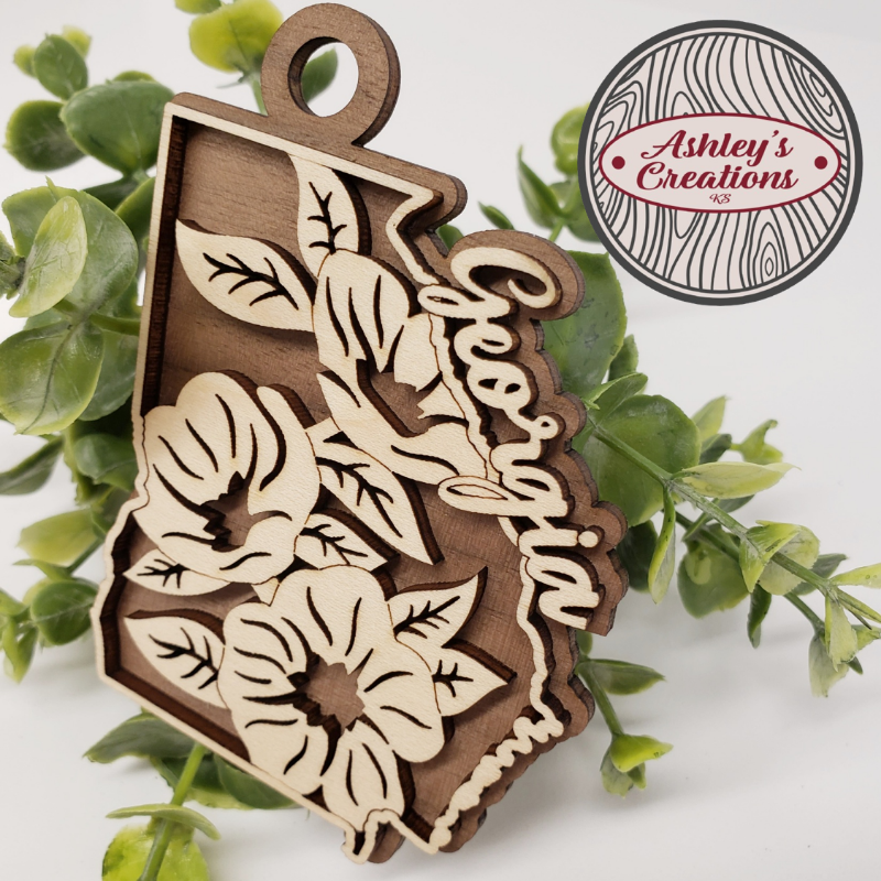 Wooden ornament shaped like the state of Georgia with floral designs on a white background.