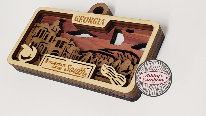 Wooden three layer license plate ornament with 'Georgia' and 'Embrace State of the South' text, featuring a silhouette of a building and guitar.