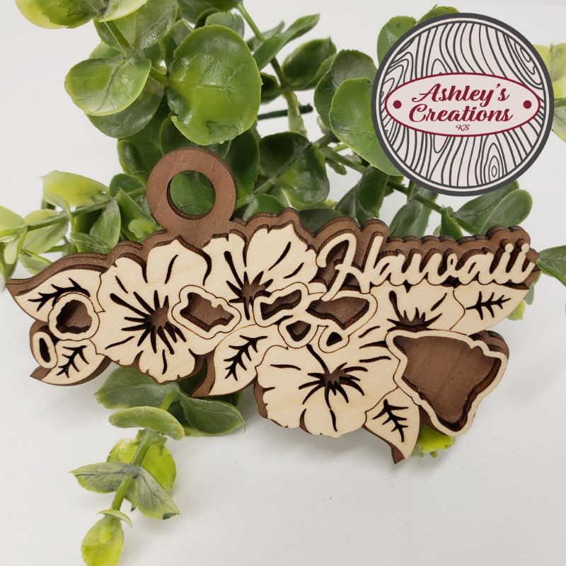 Wooden 'Hawaii' ornament with floral designs on a green leaf background, featuring 'Ashley's Creations' logo.
