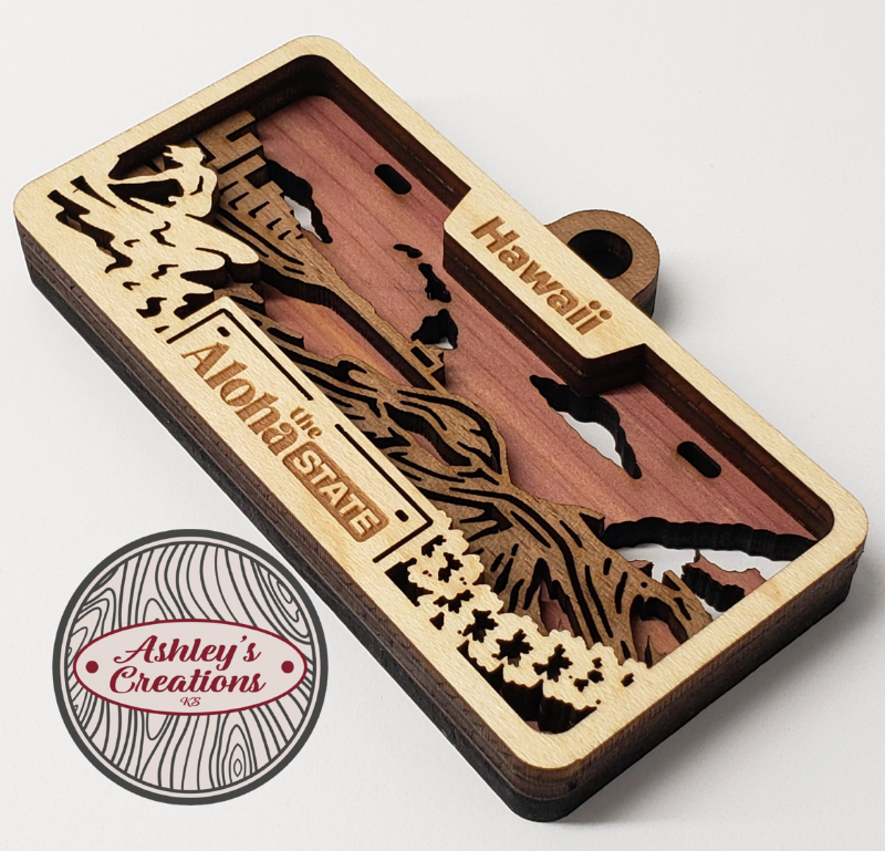 Wooden three layer license plate ornament with laser-cut designs and 'Hawaii' text, branded 'Ashley's Creations'.
