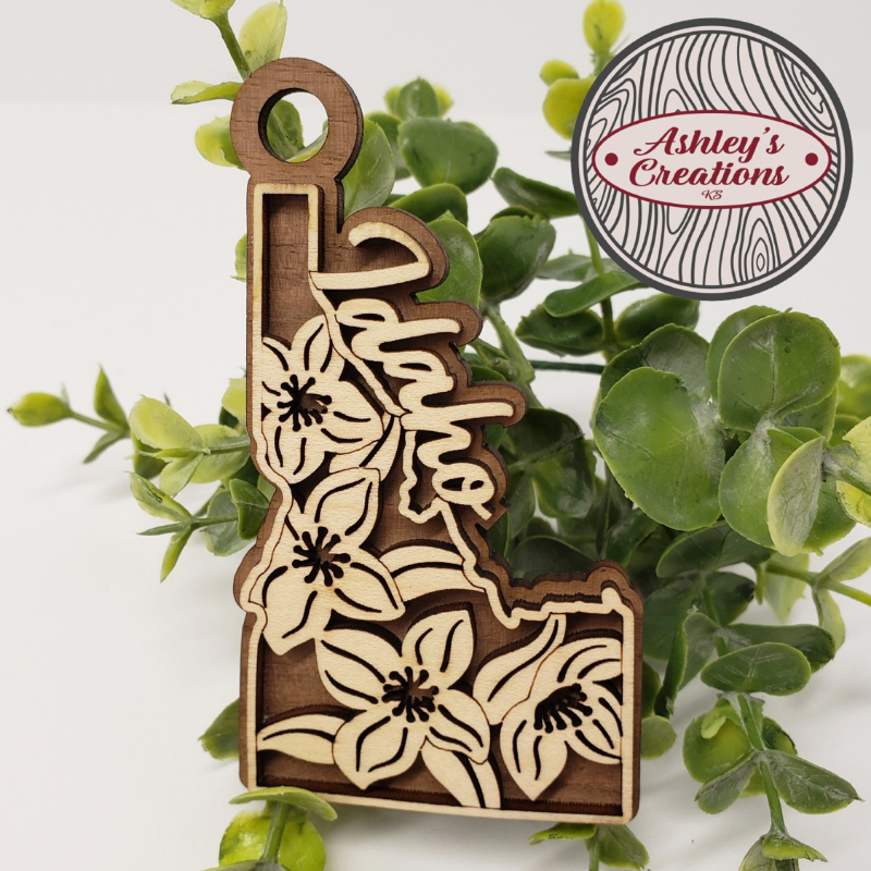 Wooden ornament shaped like a state with floral designs on a green leaf background, featuring 'Ashley's Creations' logo.