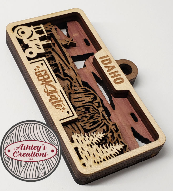Wooden three layer license plate ornament with laser-cut design and 'Idaho' text, branded 'Ashley's Creations'.