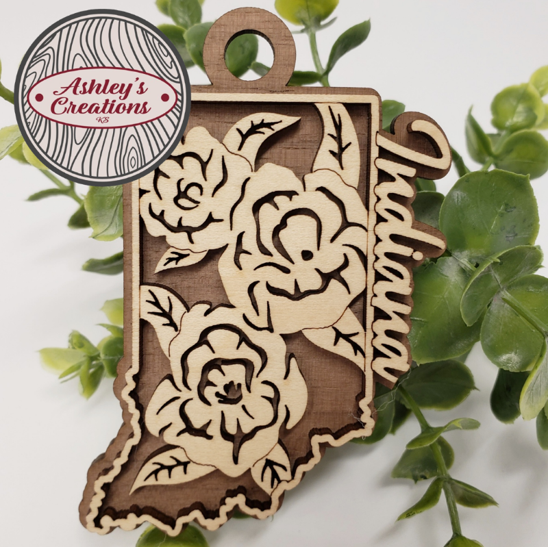 Wooden ornament shaped like the state of Indiana with floral designs on a green leaf background.