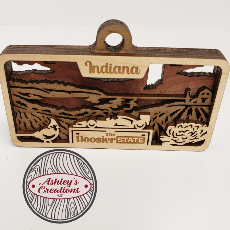 Wooden ornament item with 'Indiana' and 'Hoosier State' text, featuring a car and nature design, on a white background.