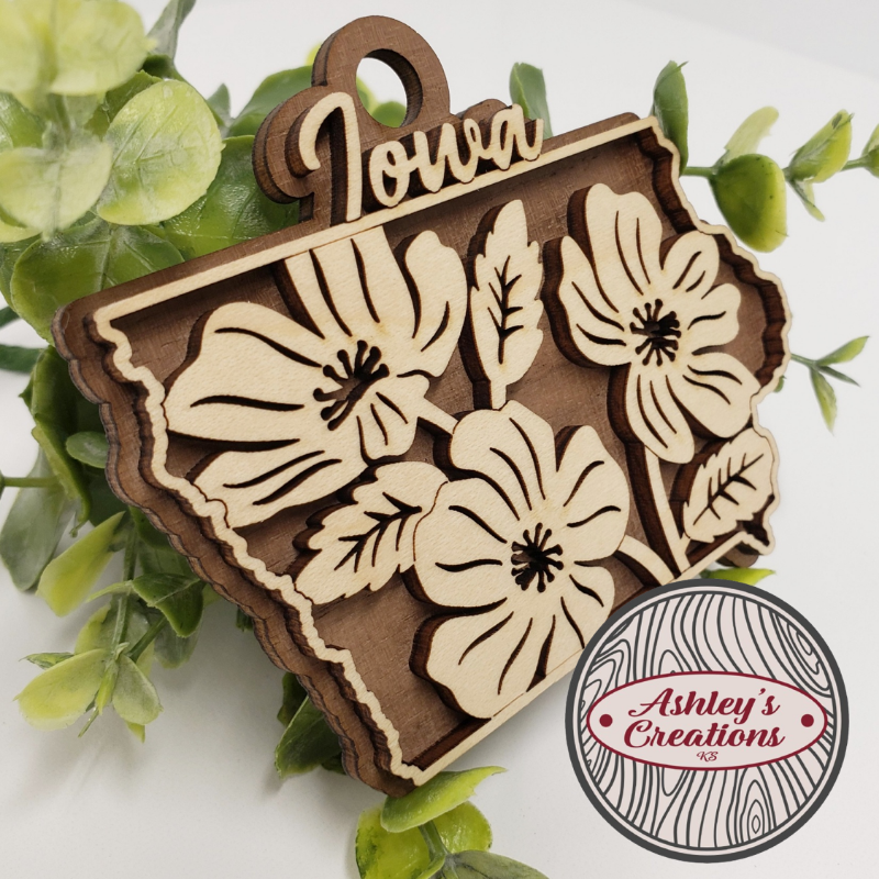 Wooden ornament shaped like the state of Iowa with floral designs on a white background.