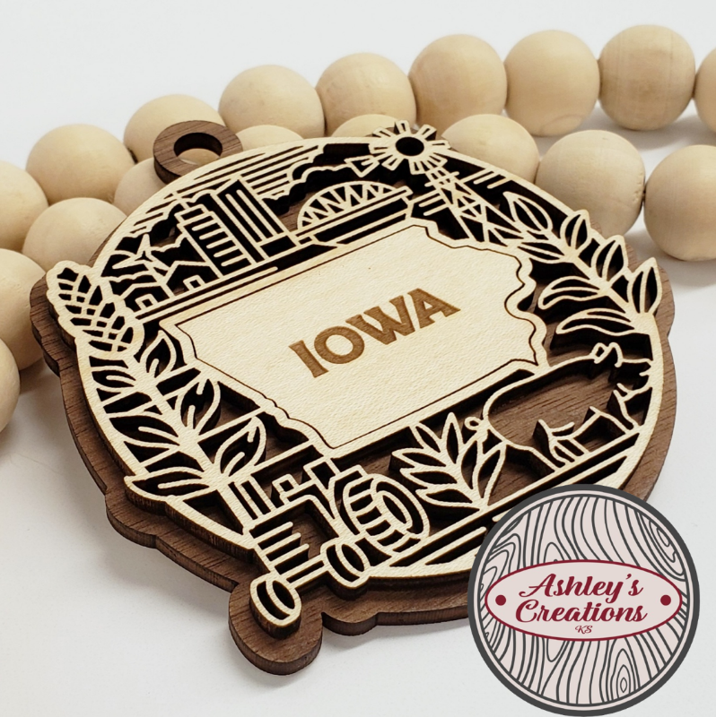 Wooden ornament with 'Iowa' engraving surrounded by wooden beads, branded 'Ashley's Creations'.