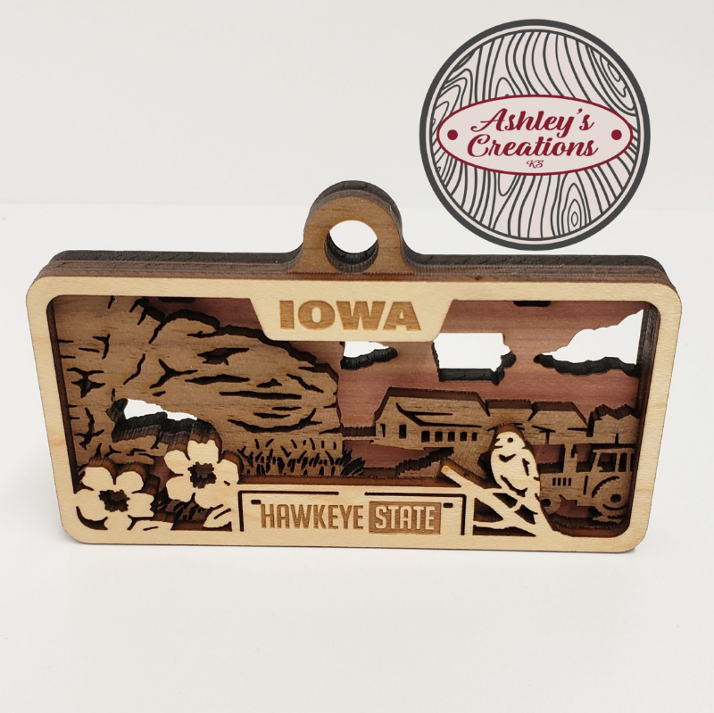 Wooden ornament with Iowa design and 'Ashley's Creations' logo.