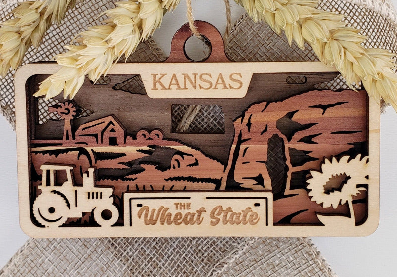 Wooden decorative sign with Kansas-themed designs and text, featuring a tractor and wheat stalks.