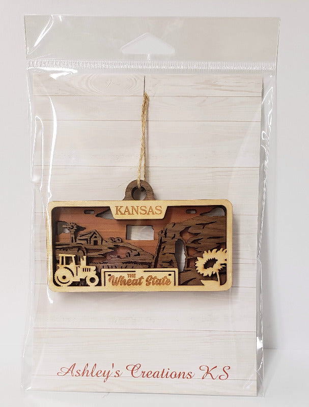Decorative ornament with 'Kansas' text and graphics in clear packaging, brand 'Ashley's Creations K.S.' visible.