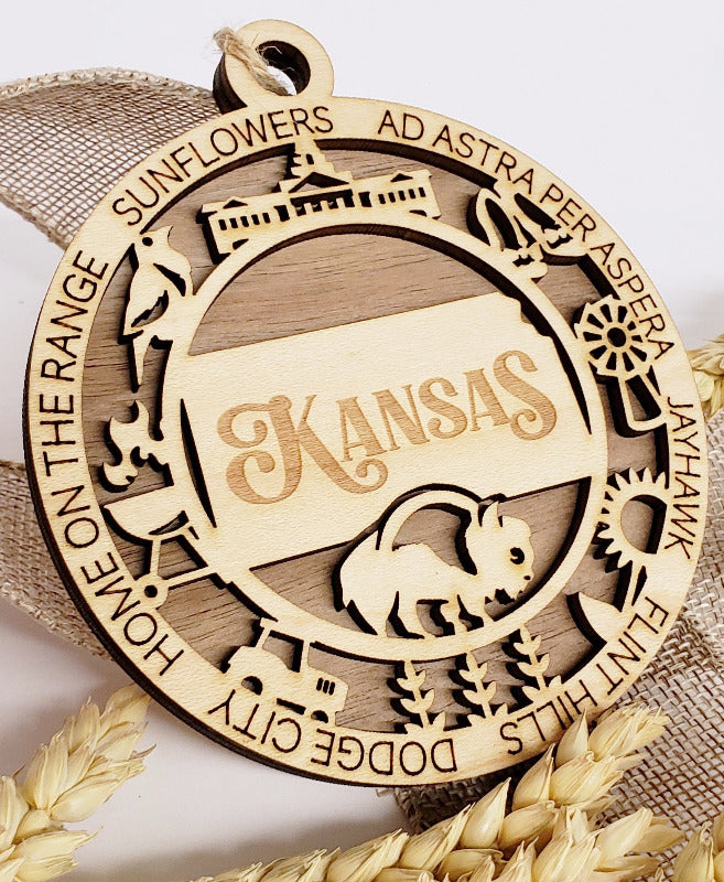 A two-layer wooden ornament with 'Kansas' and various icons laser-cut into the front layer, set against a neutral background.