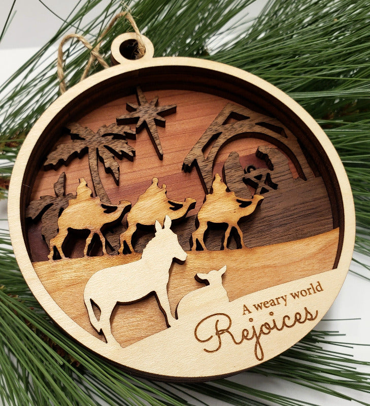 Wooden Christmas ornament with nativity scene and 'A weary world Rejoices' text on green pine needles.