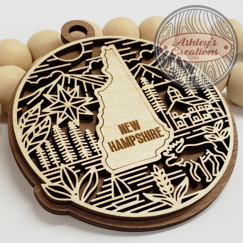 Wooden ornament with New Hampshire design and 'Ashley's Creations' branding.