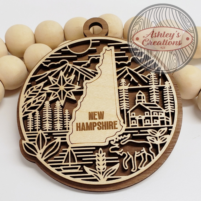 Wooden ornament with New Hampshire design and 'Ashley's Creations' branding.