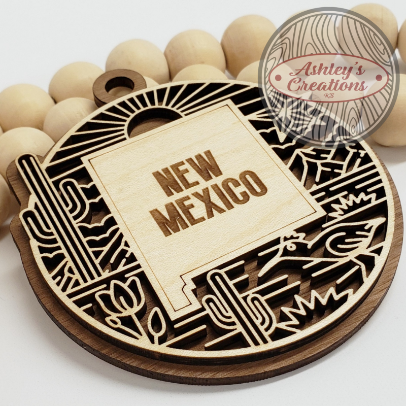 Wooden ornament with 'New Mexico' text and cactus design, branded 'Ashley's Creations'.