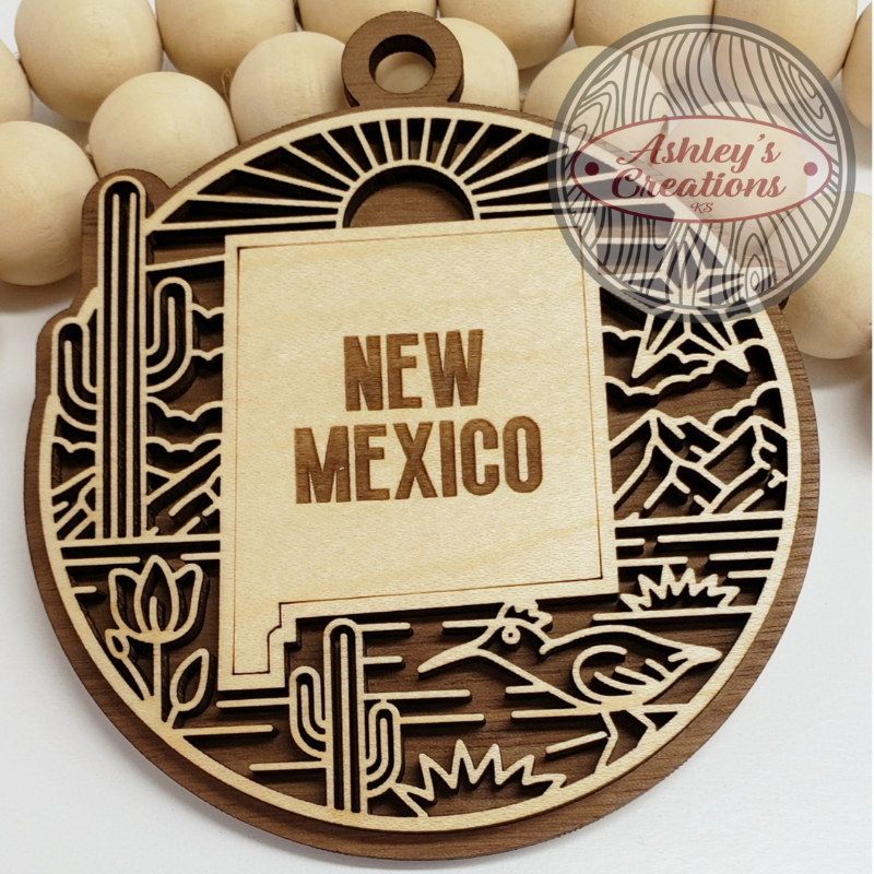 Wooden ornament with 'New Mexico' text and desert-themed design, branded 'Ashley's Creations'.