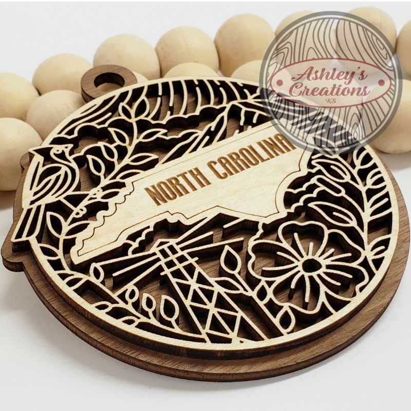 Wooden decorative item with 'North Carolina' text and intricate cut-out patterns, branded 'Ashley's Creations'.