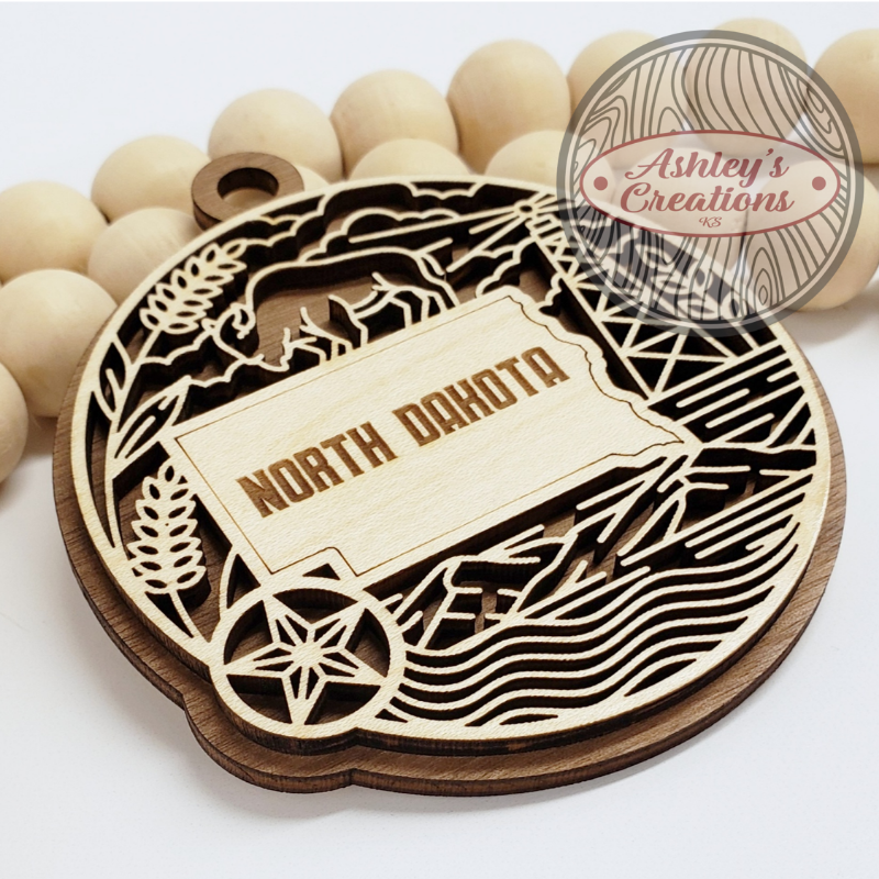 Wooden ornament with 'North Dakota' design and 'Ashley's Creations' branding.