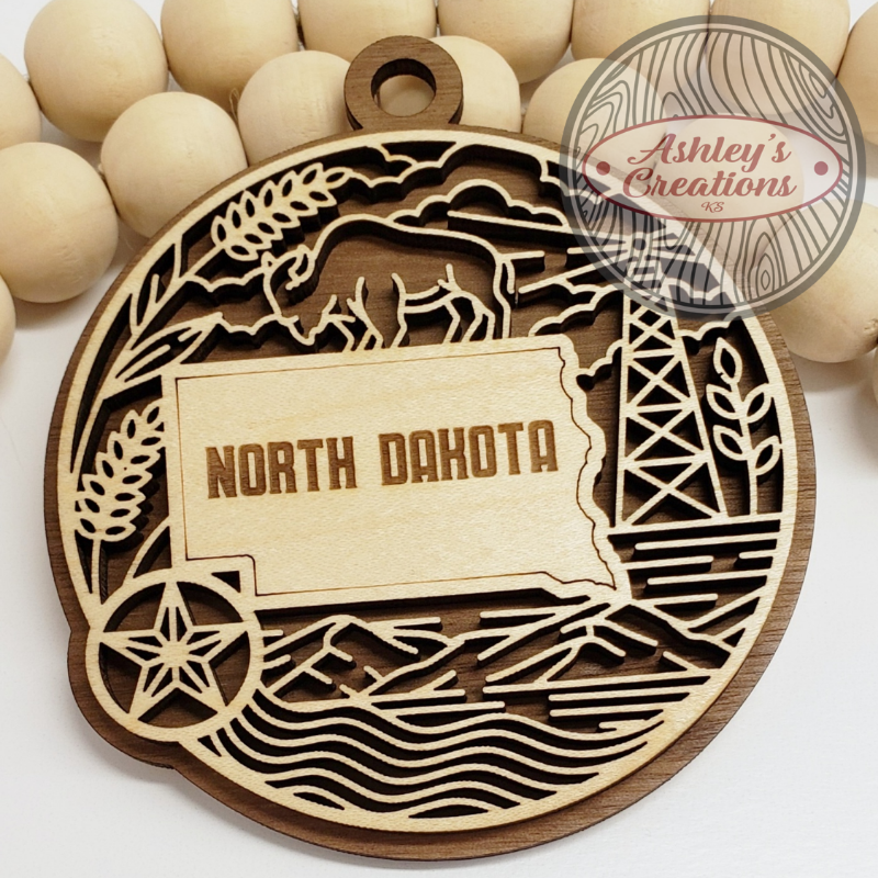 Wooden ornament with 'North Dakota' design and 'Ashley's Creations' logo.