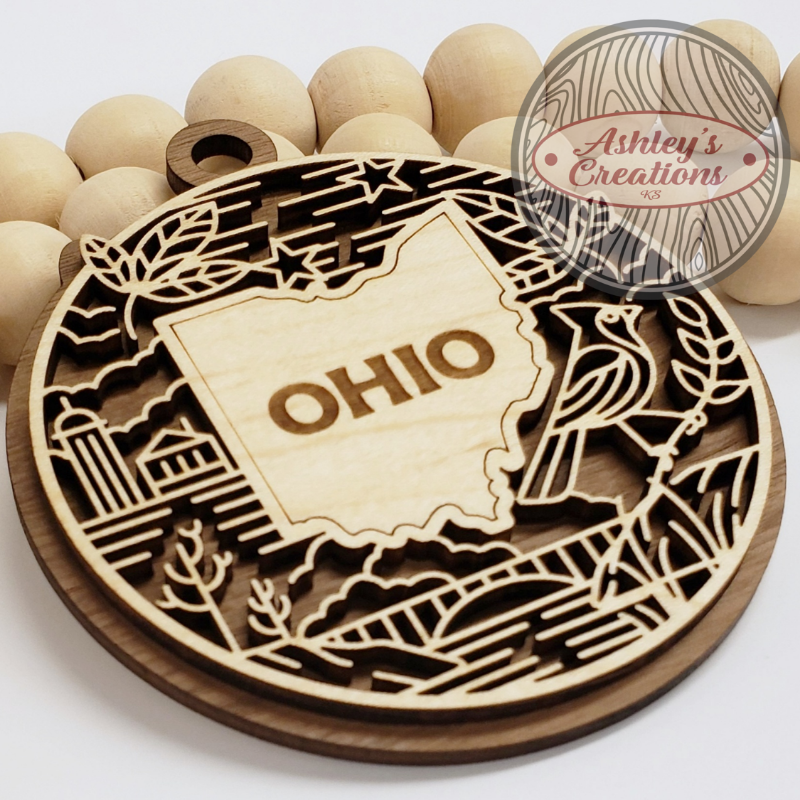 Wooden ornament with laser-cut design of Ohio and decorative elements, branded 'Ashley's Creations'.