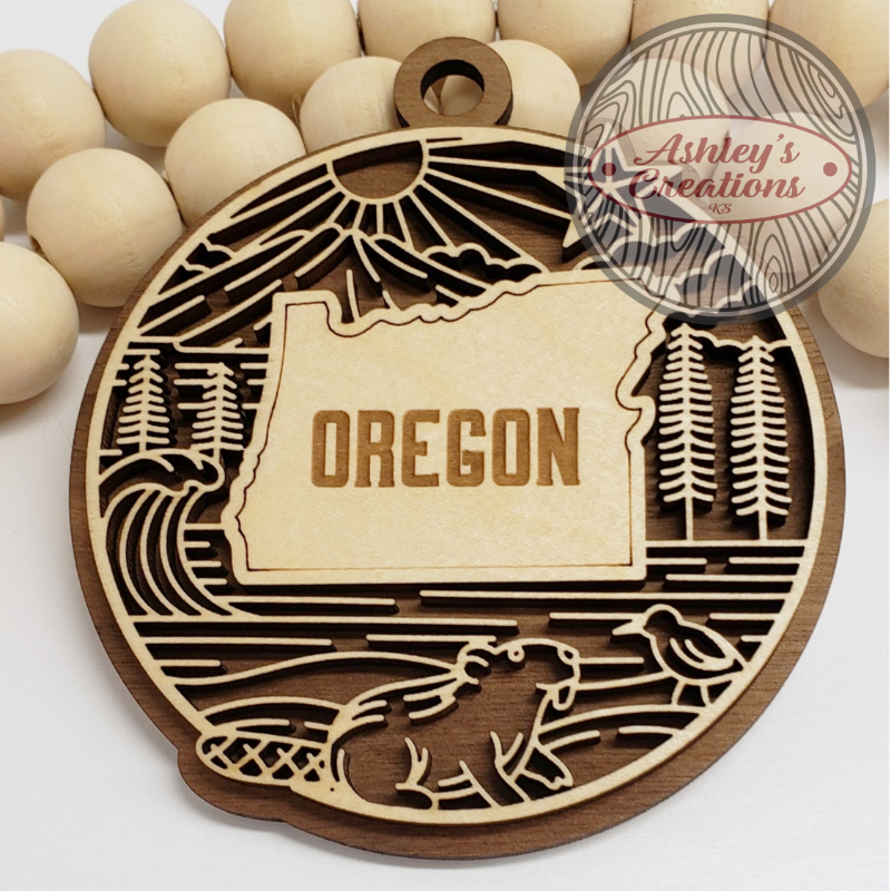 Wooden ornament with 'OREGON' engraving and nature-themed cutouts on a white background.