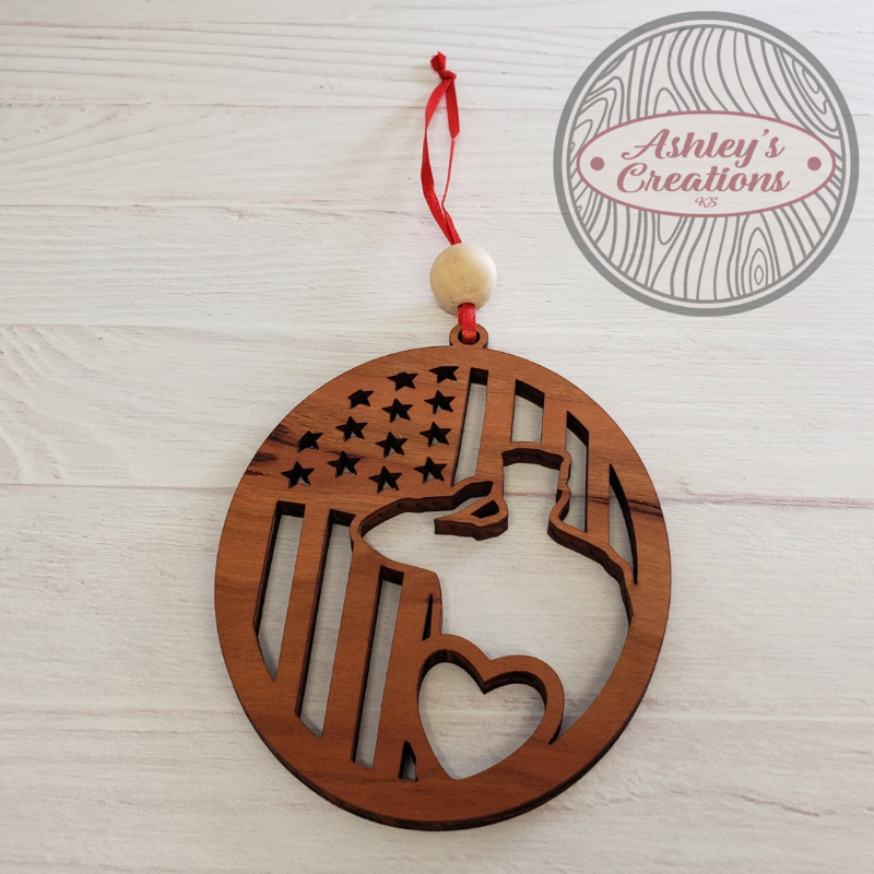 Wooden ornament with American flag and heart design, hanging on a white surface with 'Ashley's Creations' logo.