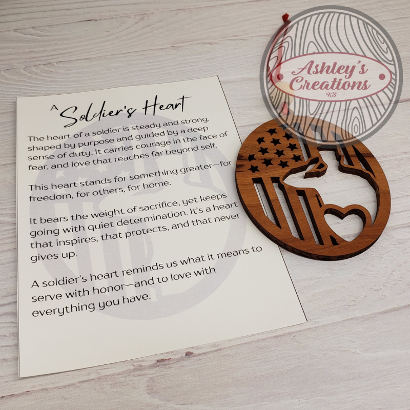 Wooden heart-shaped ornament with American flag design on a card with text, branded 'Ashley's Creations'.
