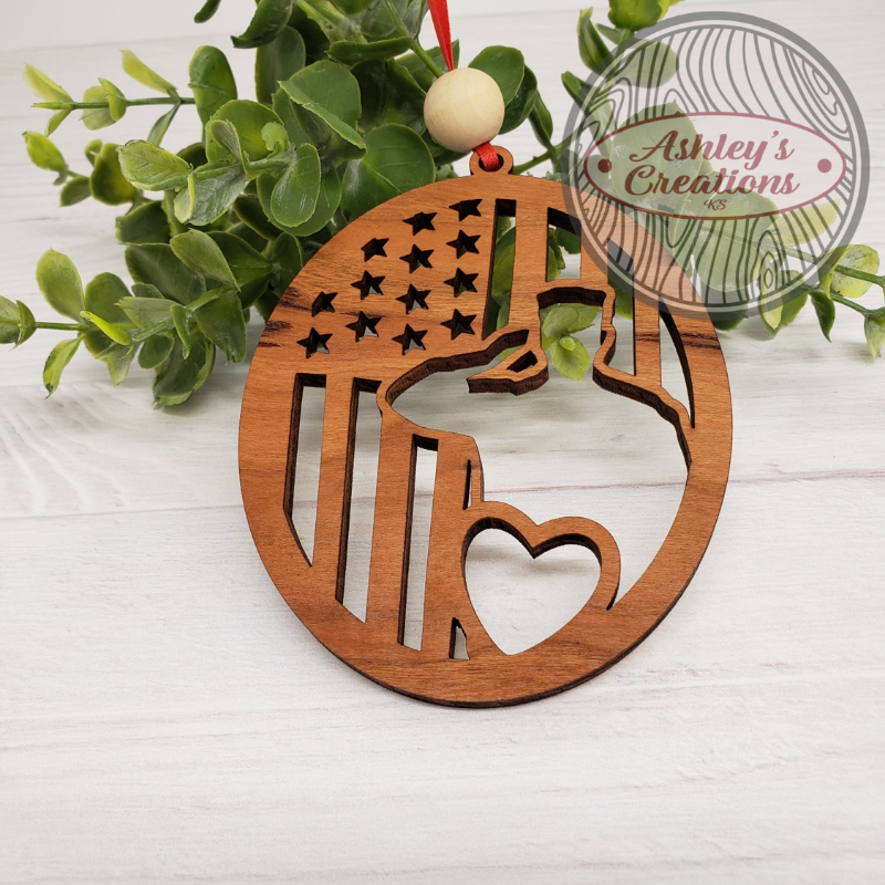 Wooden ornament with American flag design on a white surface with greenery