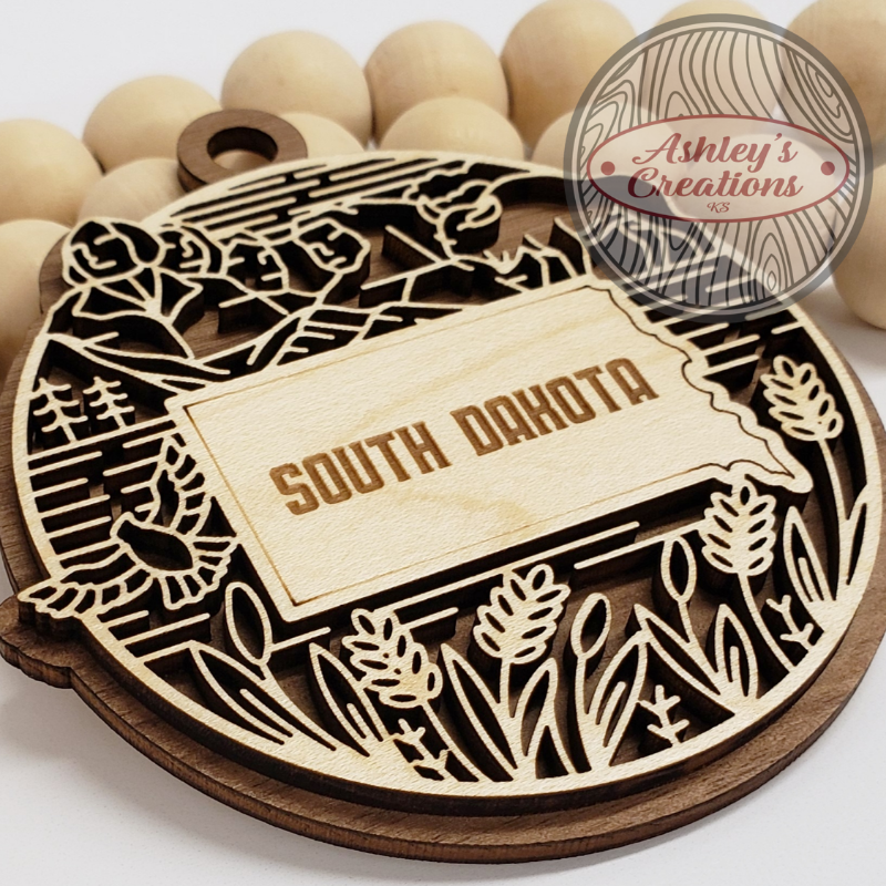 Wooden ornament with 'South Dakota' text surrounded by decorative elements on a white background.