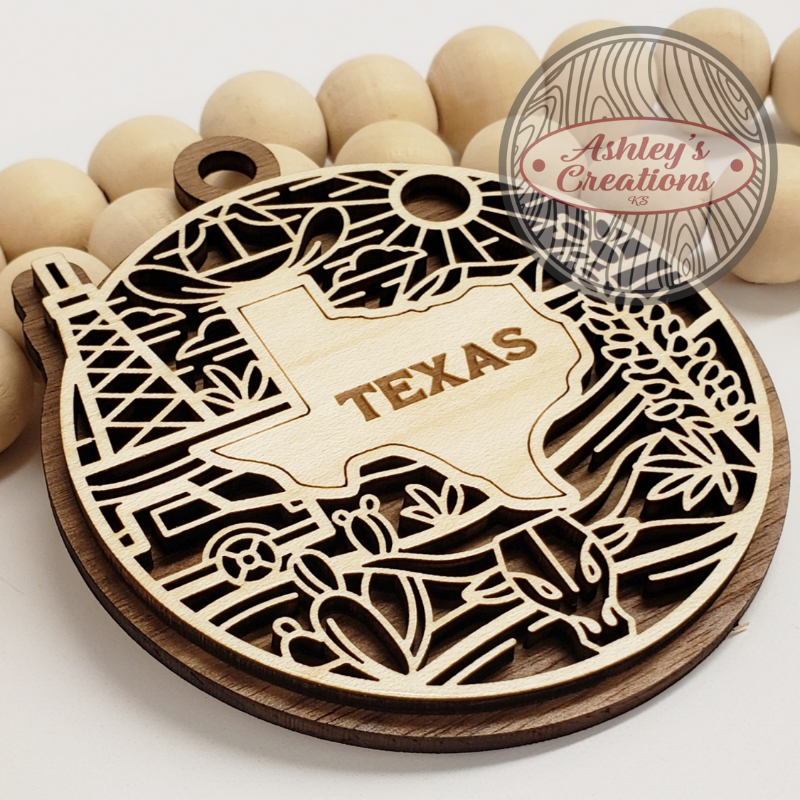Wooden ornament with 'Texas' engraving and cow design, branded 'Ashley's Creations'.