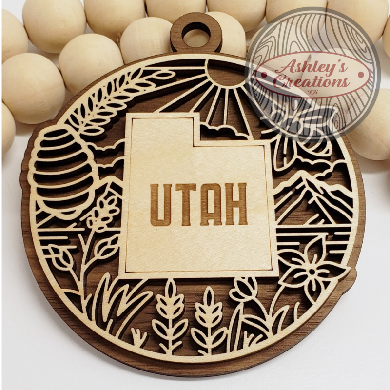 Wooden ornament with 'Utah' engraving and nature-themed design, branded 'Ashley's Creations'.
