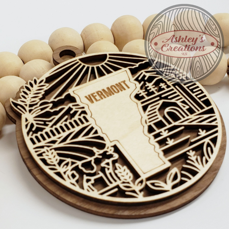 Wooden ornament with 'Vermont' engraving and decorative elements on a white background.