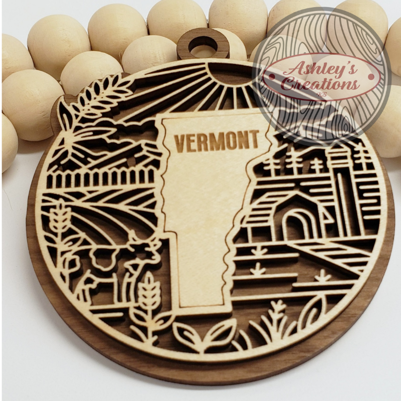 Wooden ornament with 'VERMONT' engraving surrounded by wooden beads, branded 'Ashley's Creations'.