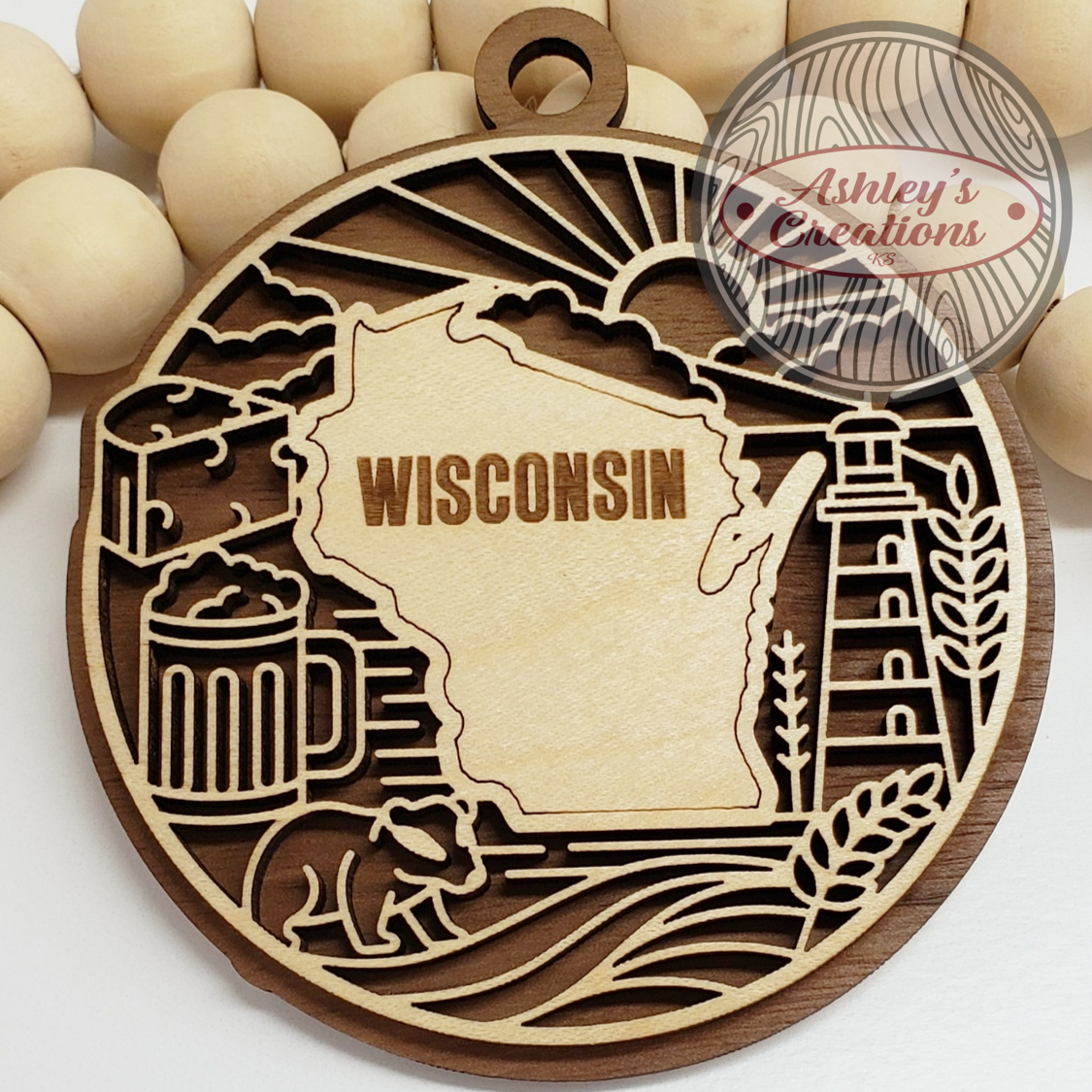 Wooden ornament with laser-cut design of Wisconsin, beer mug, and lighthouse, branded 'Ashley's Creations'.
