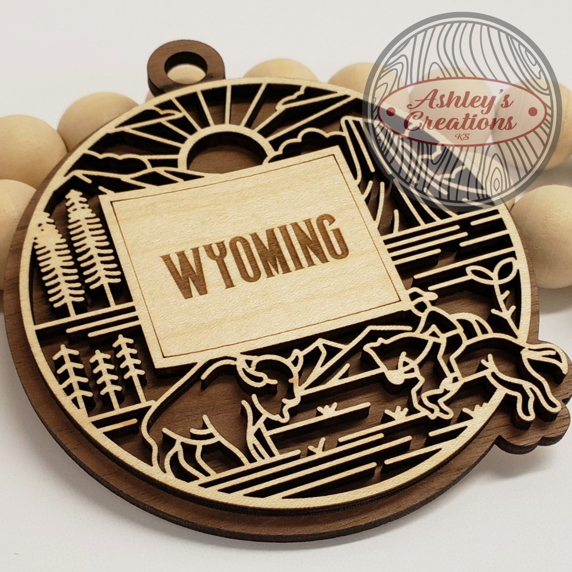 Wooden ornament with 'Wyoming' engraving and nature-themed design, branded 'Ashley's Creations'.