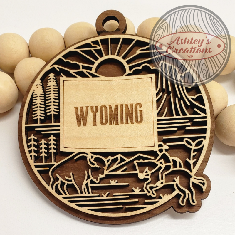 Wooden ornament with 'Wyoming' engraving and nature-themed designs, branded 'Ashley's Creations'.